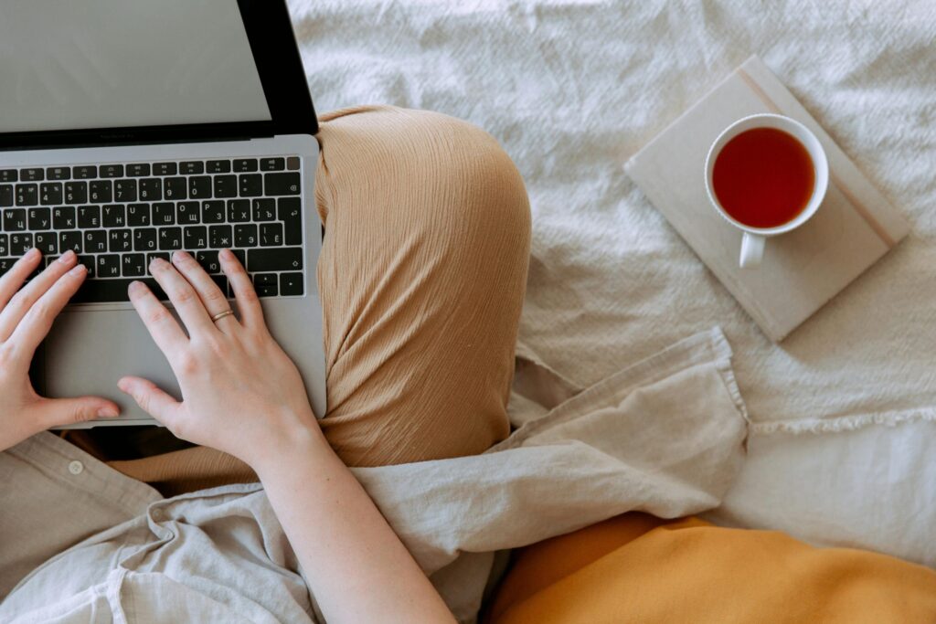 Anonymous woman in casual clothes sitting on sofa and browsing laptop with blank screen while working on project on bed